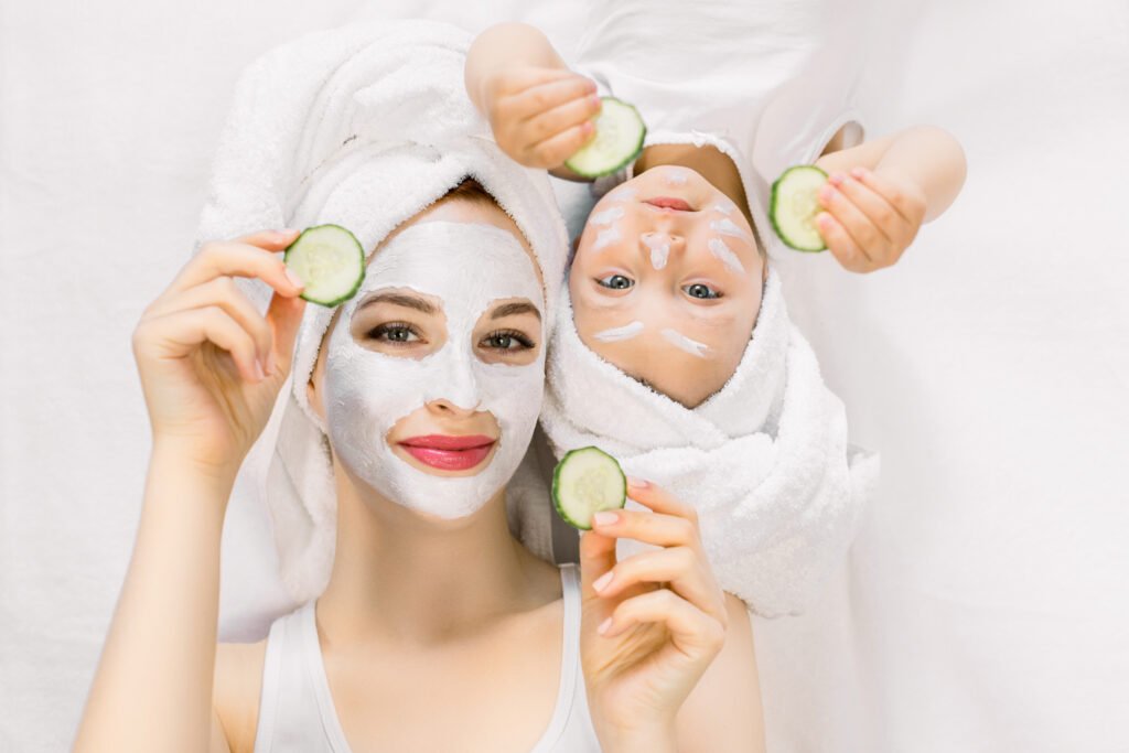 “Mother and child relaxing together with facial masks, wrapped in towels, and holding cucumber slices during a spa day.”